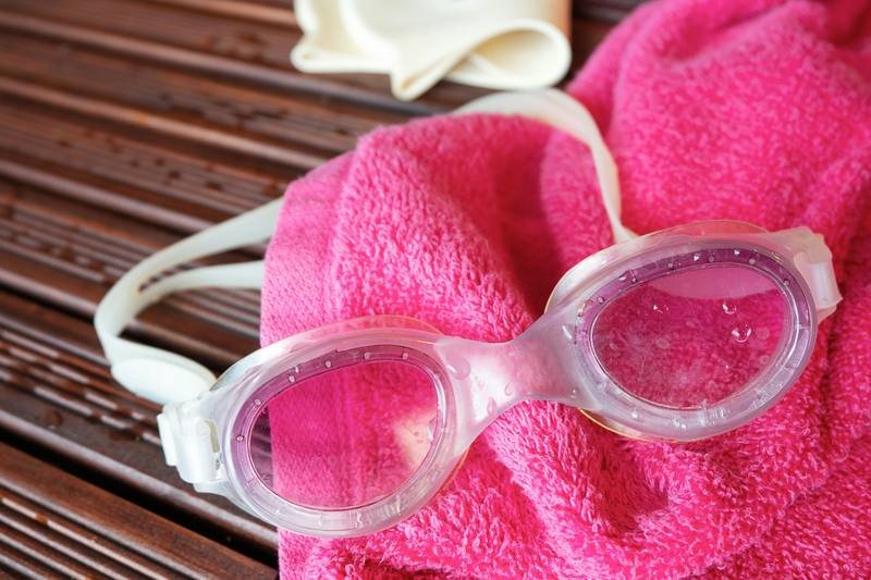 swim goggles laid out next to a towel and swim cap for a beach day