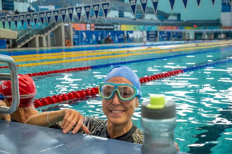 woman smiling while wearing swim goggles and cap in the pool