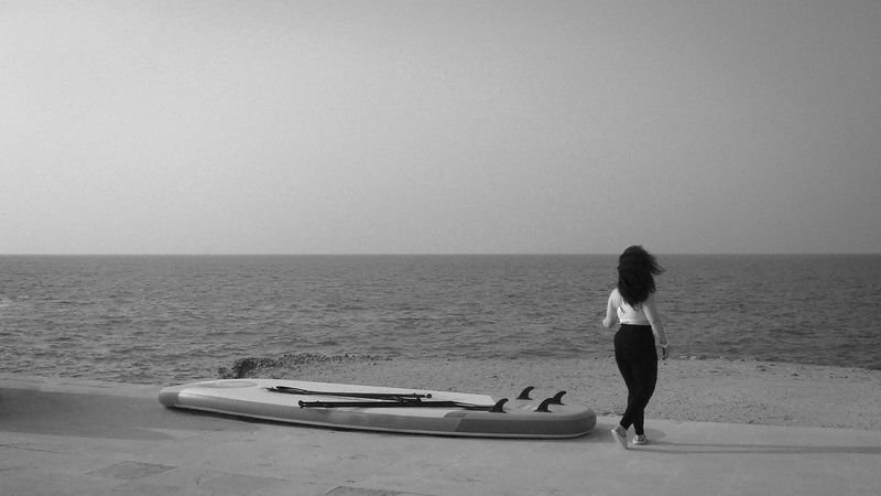 Woman in swimwear carrying a paddleboard by the shore