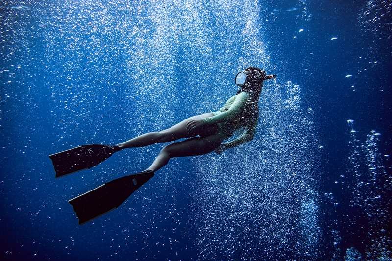 woman swimming underwater in a secure one-piece swimsuit built for freediving