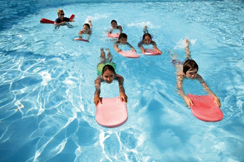 Kids playing with pool floaties while being supervised at a public pool