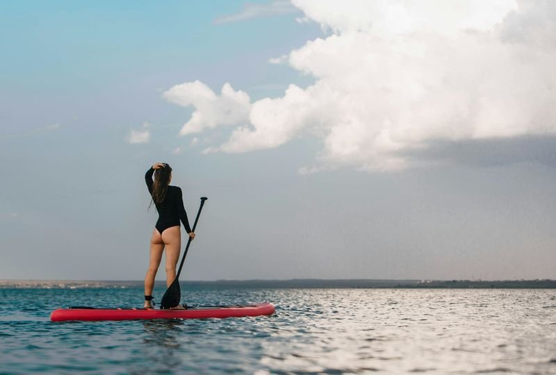 Woman in a one-piece swimsuit paddleboarding on a lake