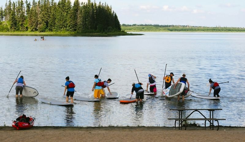 Group entering the water with stand up paddleboards on a calm lake