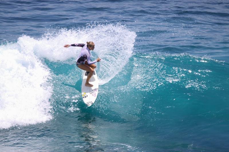 Woman in bikini surfing swimwear cutting through a wave on a surfboard