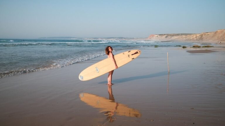 Woman carrying surfboard on the beach at sunset wearing surfing swimwear