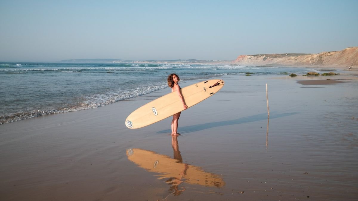 Woman carrying surfboard on the beach at sunset wearing surfing swimwear