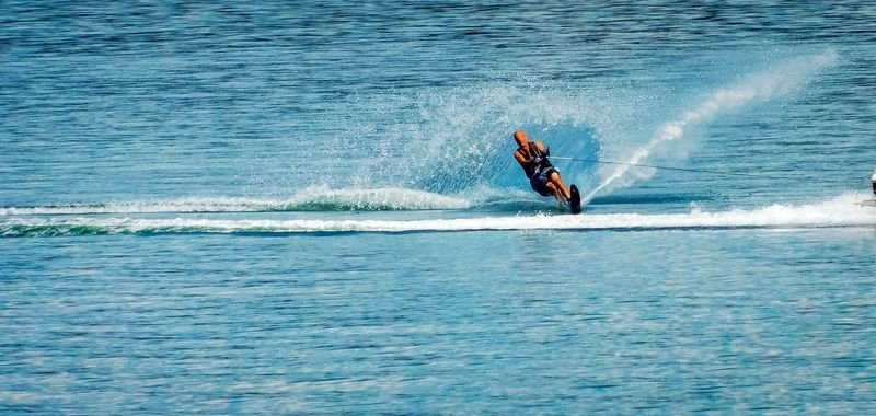 Water skier leaning into a turn behind the tow boat with spray arcing off the ski