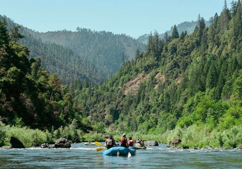 rafters in life jackets and swimwear paddling down a river