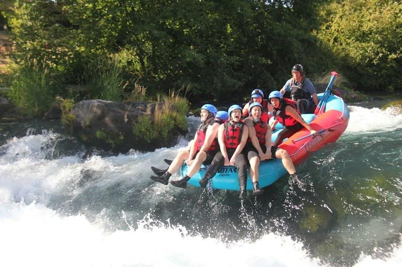 group whitewater rafting down a rocky river in swimwear and life jackets