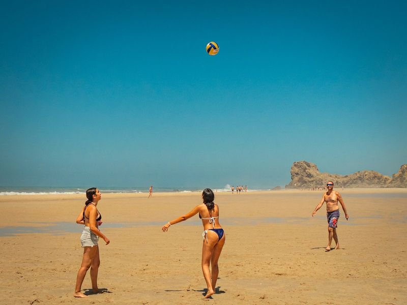 three women playing beach volleyball in bikinis on a sunny day